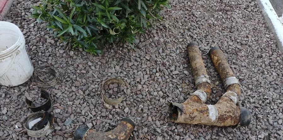 Cut sections of cast iron drain pipe removed from a Mesa property, laid on desert gravel with the corroded, scaled interior walls visible