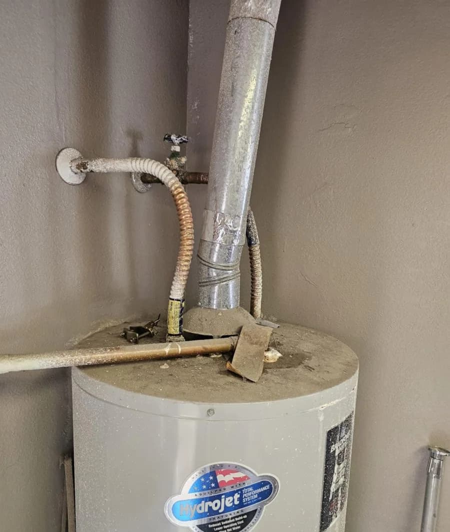The top of an aging gas water heater showing the draft hood, vent, corroded flex connectors and a dust-covered tank