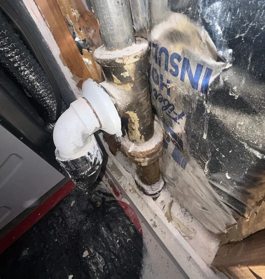 A corroded cast iron drain tee with mineral crust at both joints, exposed inside an opened wall cavity